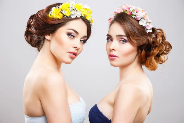 Ritratto di belle gemelle giovani donne con trucco perfetto e acconciatura con fiori nei capelli — Foto Stock