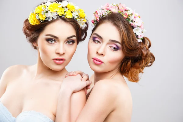 Portret piękne bliźniaki młodych kobiet z idealny makijaż i fryzura z kwiatami we włosach — Zdjęcie stockowe