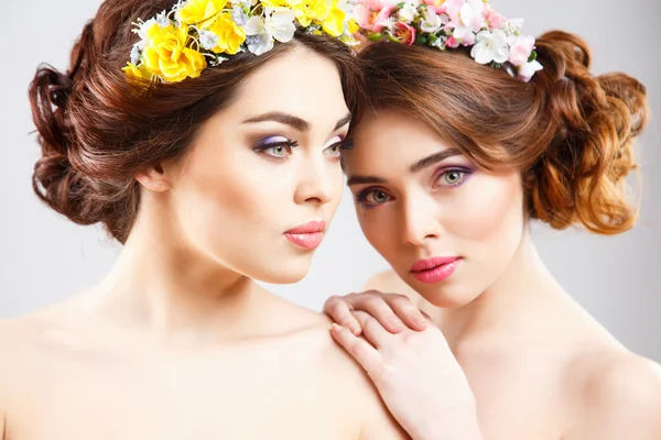 Retrato de belos gêmeos mulheres jovens com maquiagem perfeita e estilo de cabelo com flores no cabelo — Fotografia de Stock