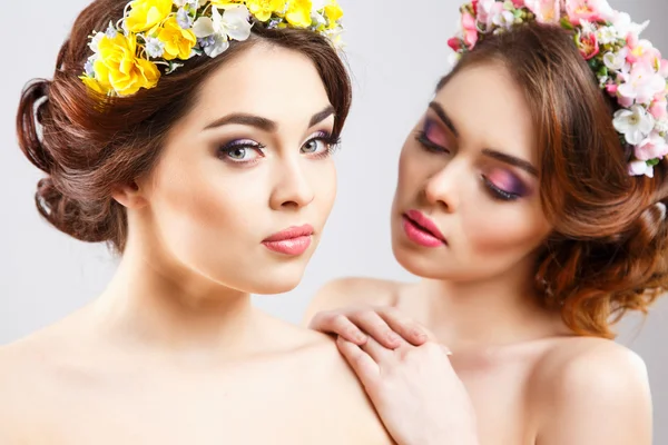 Портрет красивых близнецов молодых женщин с идеальным макияжем и прической с цветами в волосах — стоковое фото
