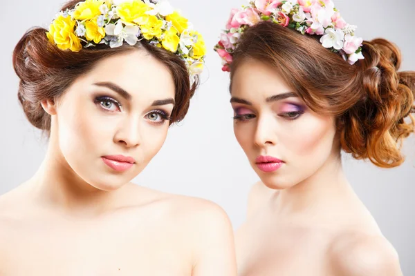 Retrato de hermosas gemelas mujeres jóvenes con maquillaje perfecto y peinado con flores en el pelo — Foto de Stock