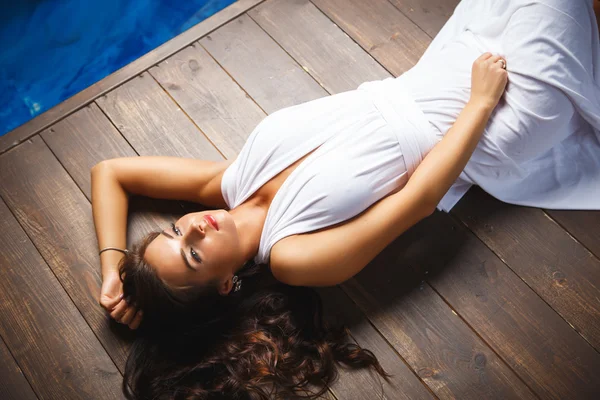 Charming young woman lying on brown wooden floor in white long dress. summer style — Stock Photo, Image