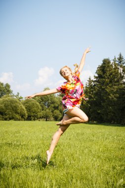 Pretty blonde young girl jumping in a park in a summer