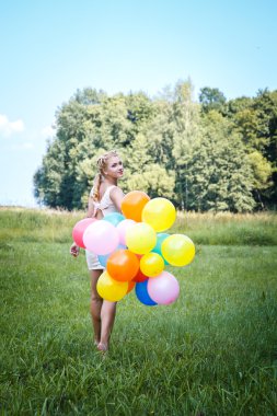 Close-up portrait of sweet young pretty blonde girl with colored make-up with many colorful balloons