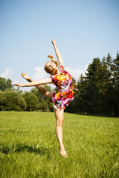 Pretty blonde young girl jumping in a park in a summer — Stockfoto
