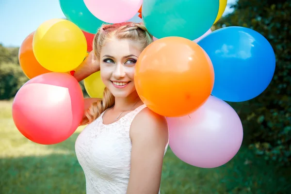 Close-up portrait of sweet young pretty blonde girl with colored make-up with many colorful balloons — Stockfoto