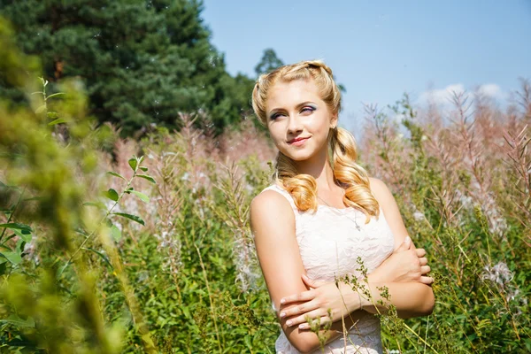 Mooie jonge blonde meisje op bloeiende veld in een zomer — Stockfoto