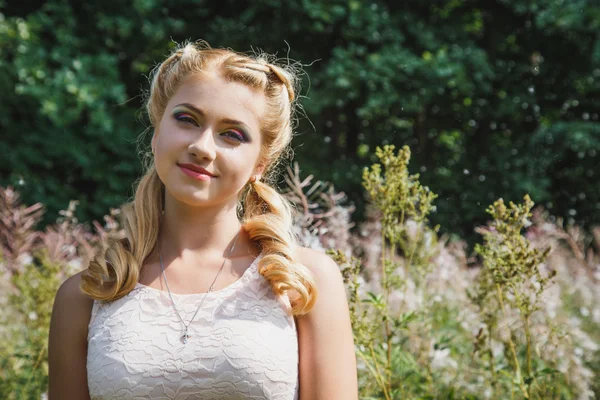 Pretty young blonde girl on blossoming field in a summer — Stock Photo, Image