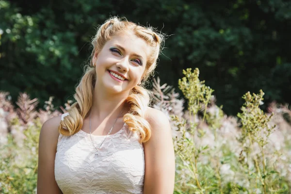 Pretty young blonde girl on blossoming field in a summer — Stock Photo, Image