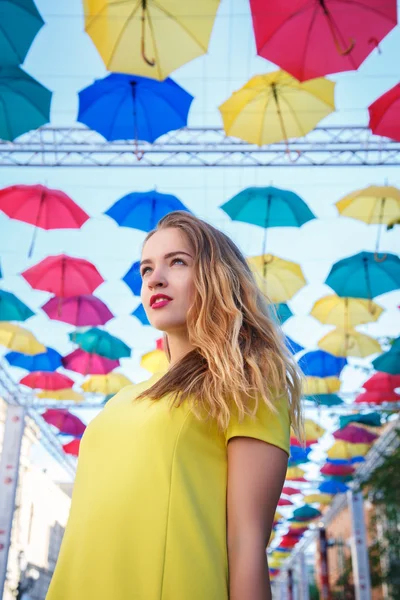 Krásná dívka ve žlutých šatech pózuje na pozadí barevné deštníky alej — Stock fotografie