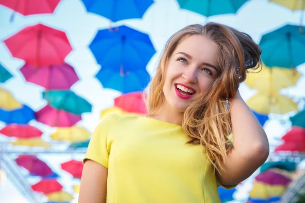 Menina bonita em vestido amarelo posando contra um fundo de guarda-chuvas multicolorido beco — Fotografia de Stock