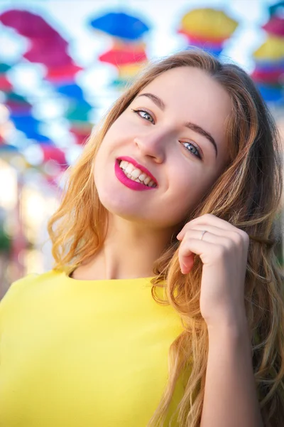 Beautiful girl in yellow dress posing against a background of multicolored umbrellas alley — Stock Photo, Image
