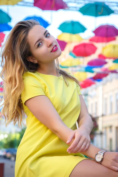 Schöne Mädchen in gelbem Kleid posiert vor einem Hintergrund von bunten Regenschirmen Allee — Stockfoto