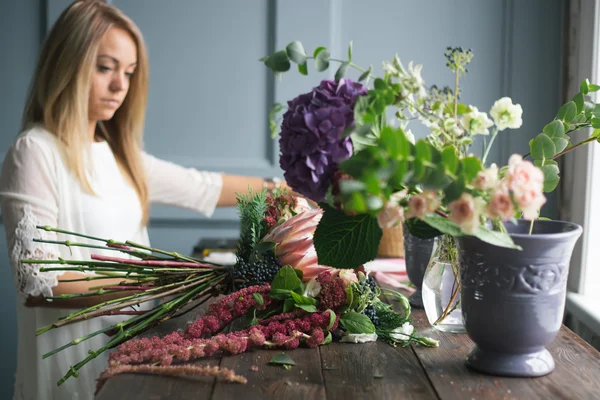 Florista en el trabajo: mujer rubia bastante joven haciendo ramo moderno de moda de diferentes flores — Foto de Stock