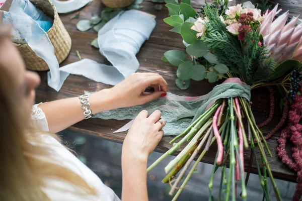 Florista en el trabajo: mujer rubia bastante joven haciendo ramo moderno de moda de diferentes flores — Foto de Stock