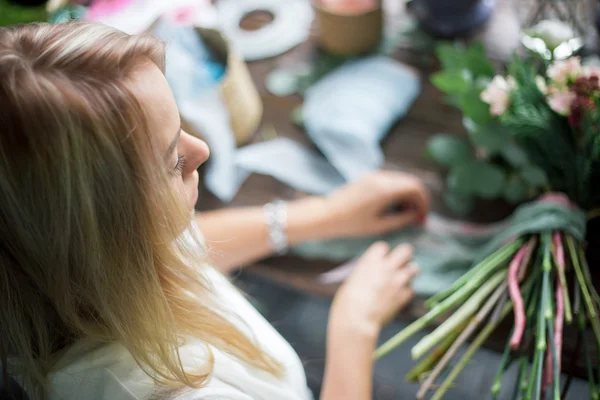 Florista en el trabajo: mujer rubia bastante joven haciendo ramo moderno de moda de diferentes flores — Foto de Stock