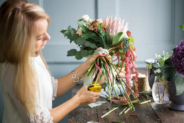 Florista en el trabajo: mujer rubia bastante joven haciendo ramo moderno de moda de diferentes flores — Foto de Stock