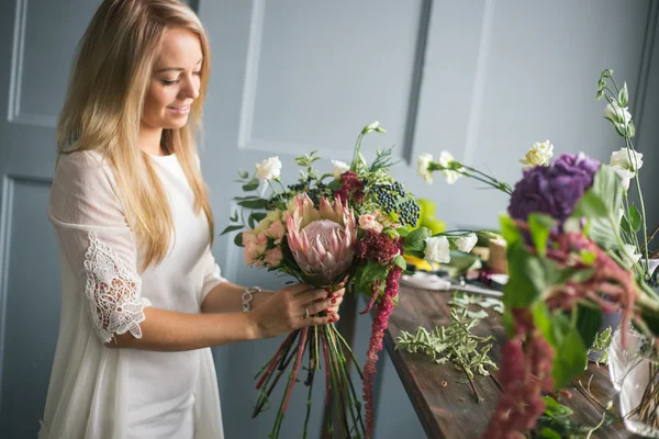 Florist at work: pretty young blond woman making fashion modern bouquet of different flowers — Stock Photo, Image