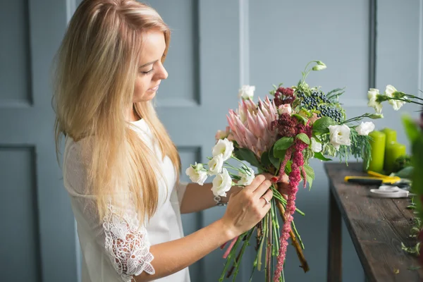 Florista en el trabajo: mujer rubia bastante joven haciendo ramo moderno de moda de diferentes flores — Foto de Stock