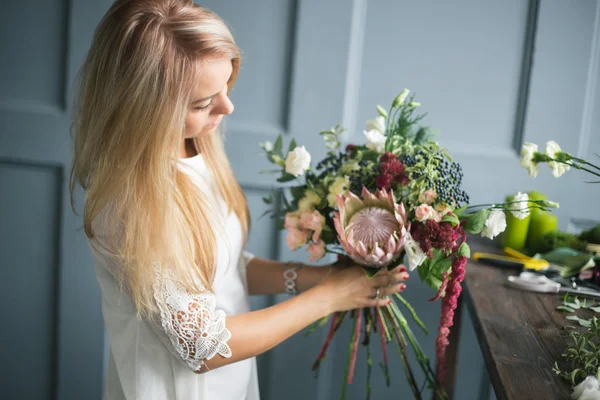 Florista no trabalho: mulher loira muito jovem fazendo moda buquê moderno de flores diferentes — Fotografia de Stock