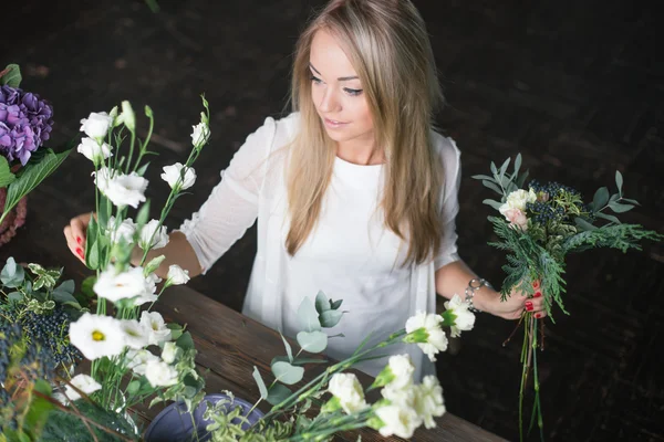 Florista en el trabajo: mujer rubia bastante joven haciendo ramo moderno de moda de diferentes flores — Foto de Stock