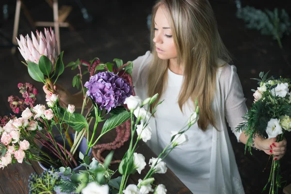 Florista en el trabajo: mujer rubia bastante joven haciendo ramo moderno de moda de diferentes flores — Foto de Stock