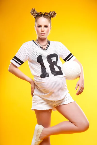 Futbol topuyla - sarı bir arka plan üzerinde izole güzel hamile kadın — Stok fotoğraf