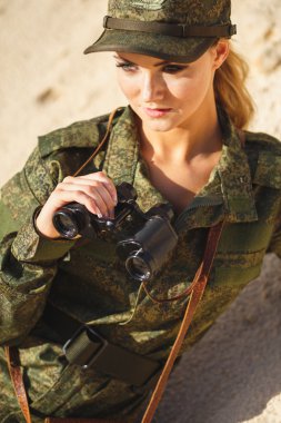 Güzel genç kadın bir tatlı arka plan üzerinde bir dürbün ile askeri bir kostüm