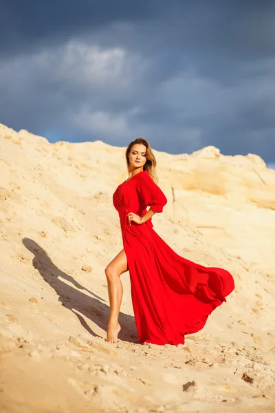 Великолепная рыжая молодая женщина в длинном красном платье в десерте. Песчаный каньон. Стиль моды — стоковое фото
