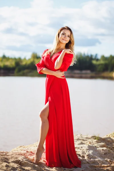 Gorgeous red head young woman in long red dress on a background of a lake. Sandy canyon. Fashion style — Stock Photo, Image