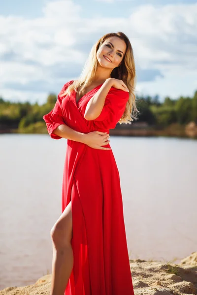 Linda cabeça vermelha jovem mulher em vestido vermelho longo em um fundo de um lago. Canyon arenoso. Estilo de moda — Fotografia de Stock