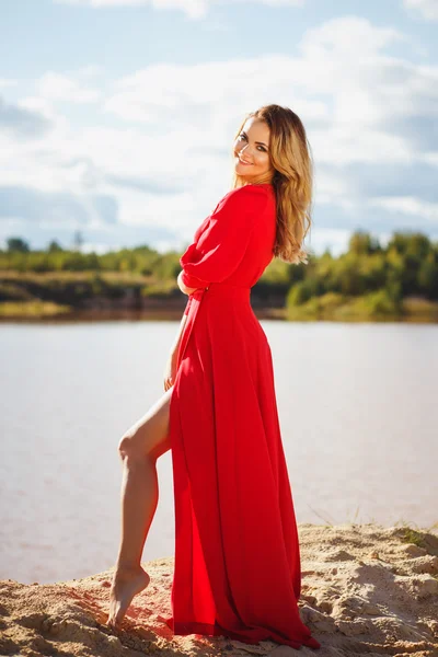 Underbara röda huvud ung kvinna i långa röda klänning på en bakgrund av en sjö. Sandy canyon. Klädstil — Stockfoto