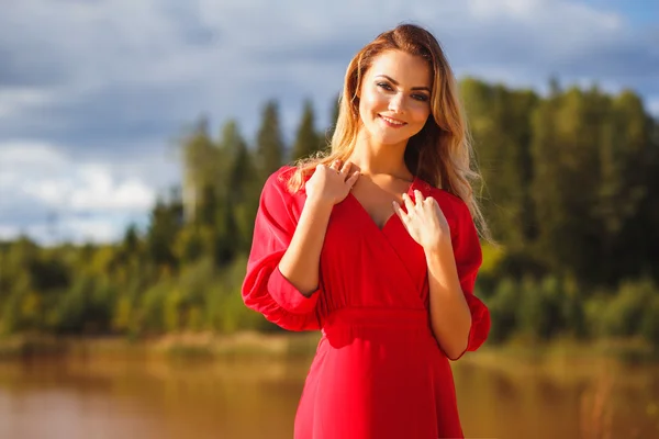 Nádherné červené hlavy mladá žena v dlouhé červené šaty na pozadí jezera. Sandy kaňonu. Módní styl — Stock fotografie