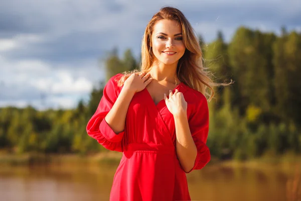 Nádherné červené hlavy mladá žena v dlouhé červené šaty na pozadí jezera. Sandy kaňonu. Módní styl — Stock fotografie