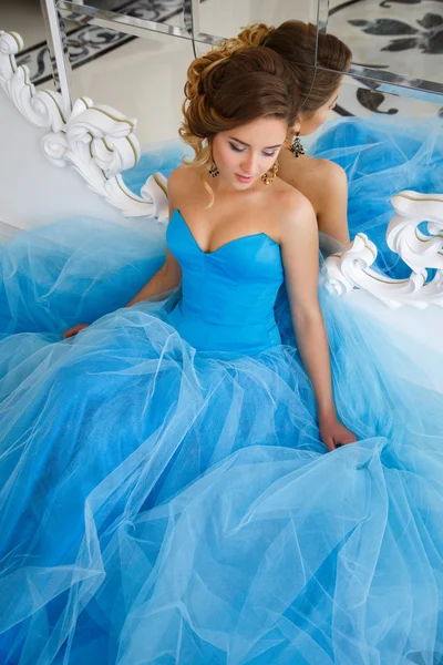 Красивая невеста в великолепном голубом платье в стиле Золушки утром, сидя рядом с зеркалом — стоковое фото