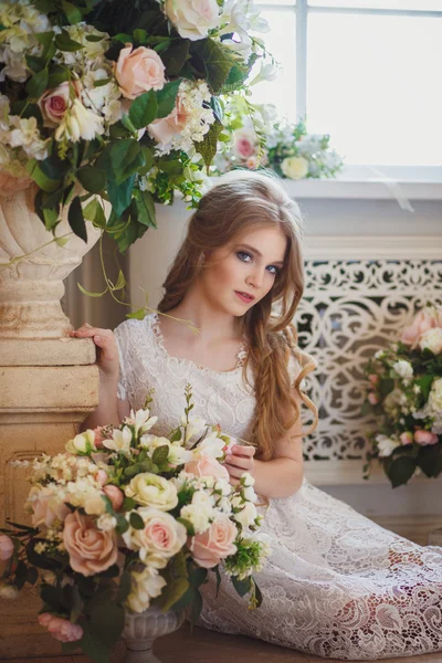 Ritratto di bella giovane ragazza in abito bianco e lunghi capelli biondi circondata da fiori — Foto Stock