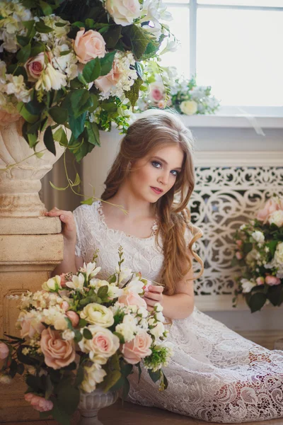 Portrait of pretty young girl in a white dress and long blonde hair surrounded by flowers — Zdjęcie stockowe