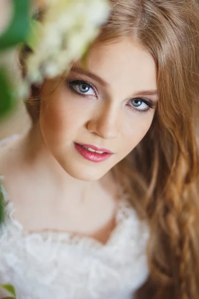 Portrait of pretty young girl in a white dress and long blonde hair surrounded by flowers — Stock Photo, Image