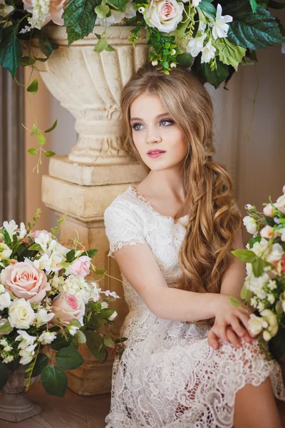 Ritratto di bella giovane ragazza in abito bianco e lunghi capelli biondi circondata da fiori — Foto Stock