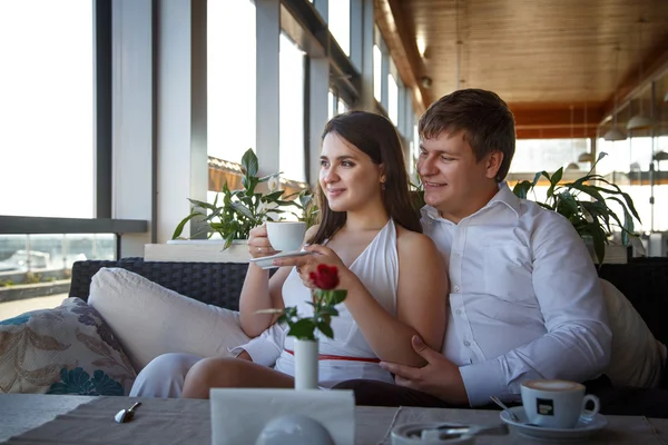 Hezká mladá bruneta žena v bílých šatech a mladý muž odpočívající společně v restauraci v letní den — Stock fotografie