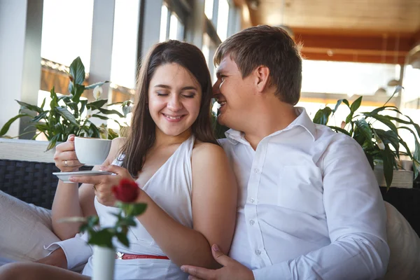 Hezká mladá bruneta žena v bílých šatech a mladý muž odpočívající společně v restauraci v letní den — Stock fotografie