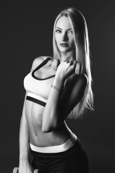 Close-up portrait of sport young blonde woman with dumbbells over dark background isolated. Fitness model. Black and white photo — Zdjęcie stockowe