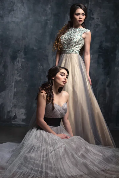 Mode schoonheid portret van prachtige jonge twins vrouwen met lang krullend haar in luxe avond jurken — Stockfoto