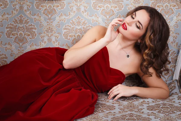 Bella giovane donna con il trucco perfetto e lo stile dei capelli in splendido abito da sera rosso in costosi interni di lusso — Foto Stock