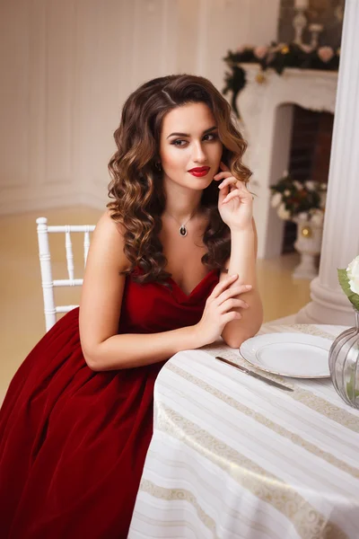 Gros plan portrait de belle jeune femme en magnifique robe de soirée en velours rouge assis à la table dans un intérieur cher — Photo