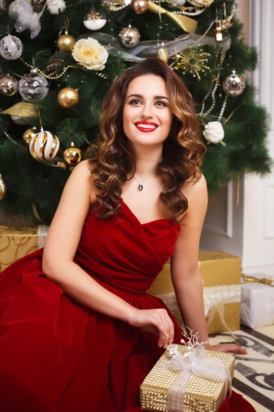 Beautiful young woman with perfect make up and hair style in gorgeous red evening dress over christmas background — Stock Photo, Image