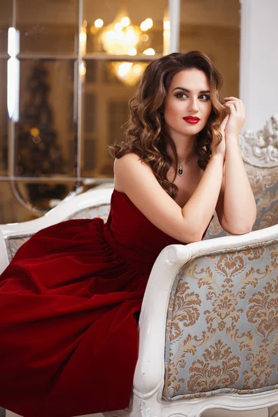Όμορφη νεαρή γυναίκα με το τέλειο μακιγιάζ και χτένισμα, στο πανέμορφο κόκκινο φόρεμα βράδυ στο εσωτερικό πανάκριβη πολυτέλεια — Φωτογραφία Αρχείου