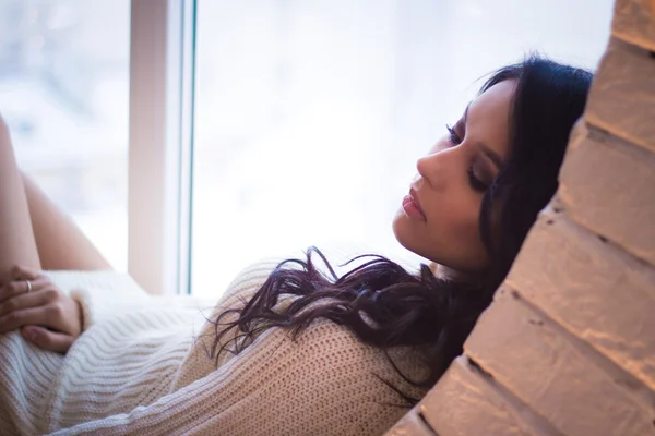 Pretty young brunette woman in white winter clothes on a round window — Stock Photo, Image