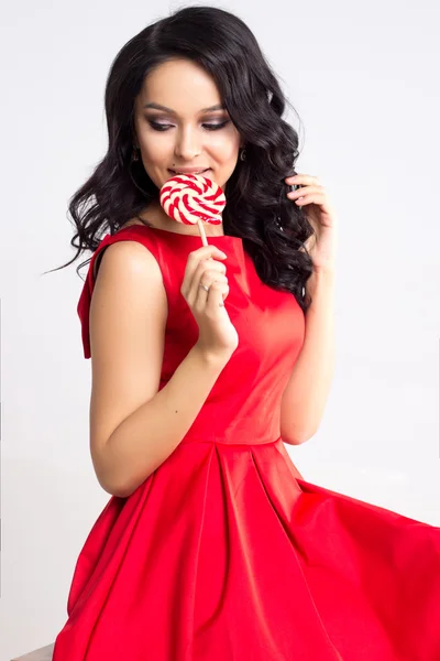 Pretty young woman in red dress with a lollipop — Stock Photo, Image