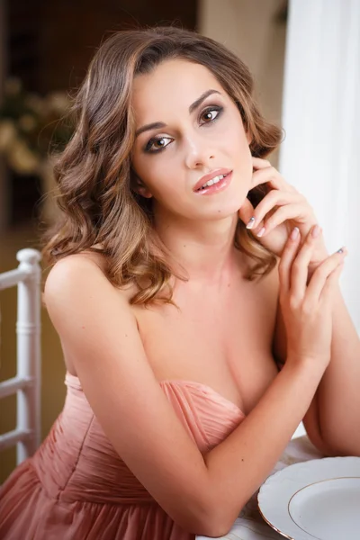 Close-up portrait of beautiful young woman in pretty beige evening dress sitting by the table in expensive interior — Stockfoto